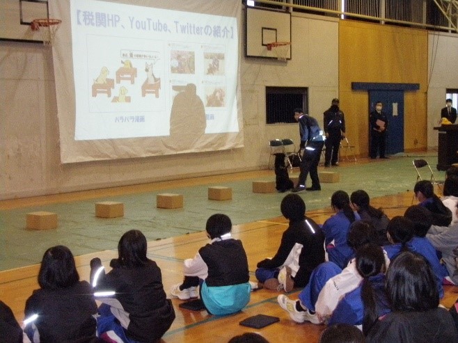 体育館での講演の様子。生徒と麻薬探知犬が写っている。