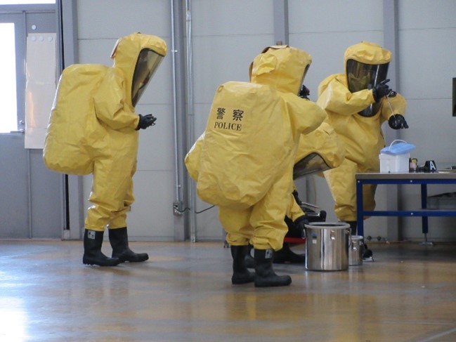 防護服を着用した警察官が不審物を処理する様子